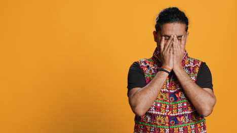 Anxious-man-covering-face-with-palms,-feeling-worried,-studio-background