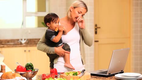 mujer en la cocina lidiando con el bebé y la computadora portátil y el teléfono