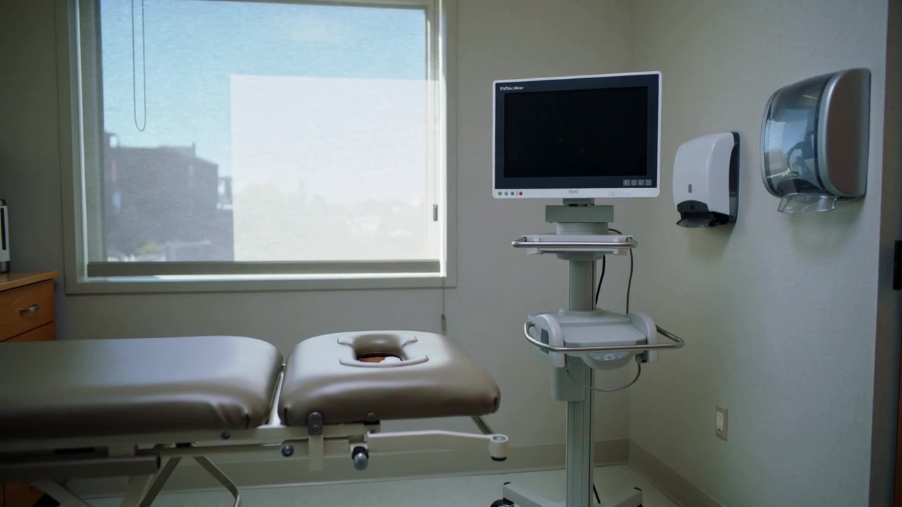 Panning camera showing padded medical examination table in clinic exam room, highlighting monitor
