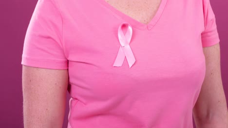 Video-of-midsection-of-caucasian-woman-wearing-pink-cancer-awareness-ribbon,-with-pink-background