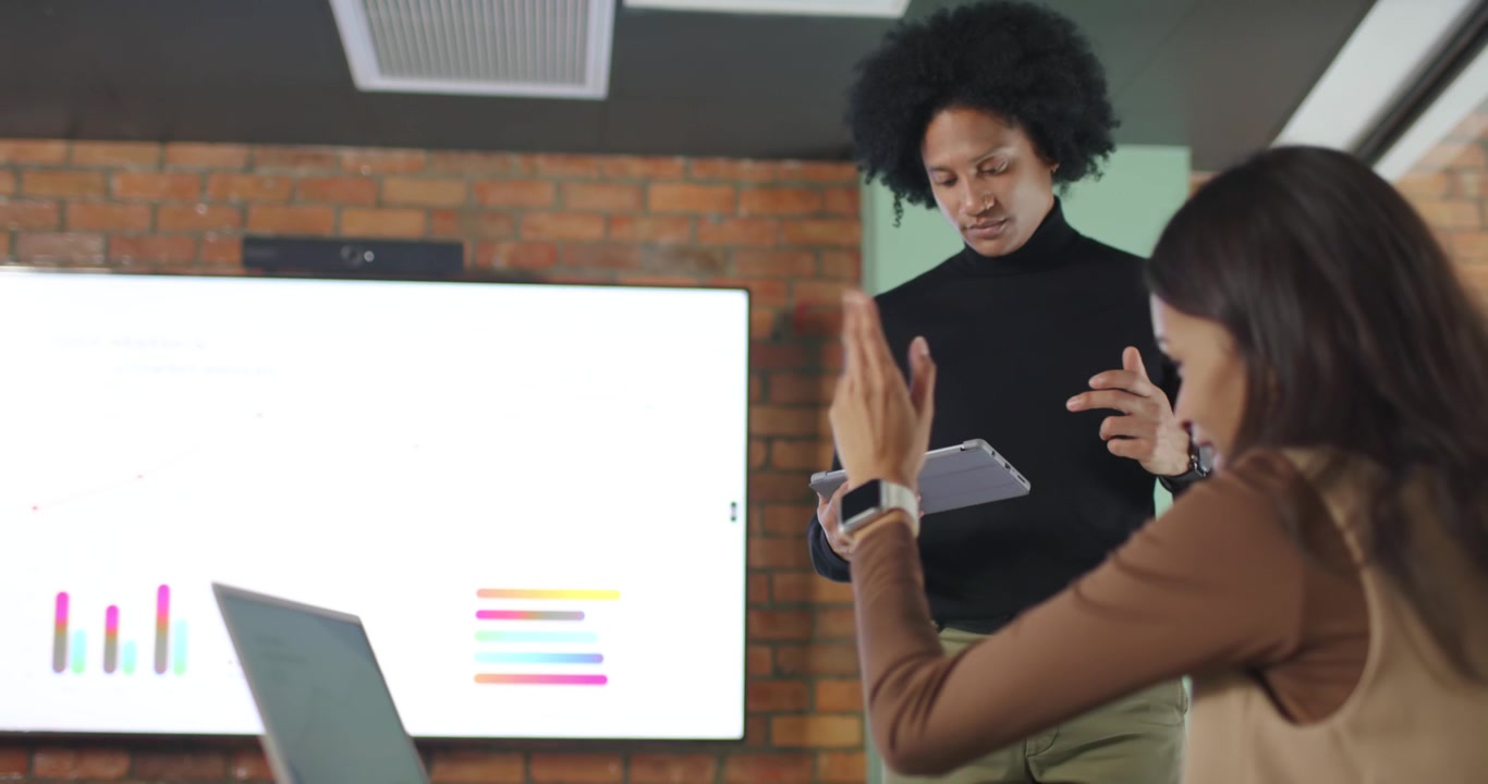 African American colleagues presenting, woman gesturing at chart display while man tapping tablet