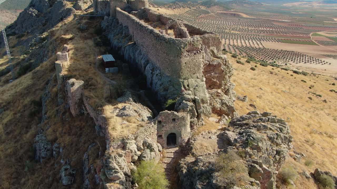 Il drone sale e si allontana sopra il Castello di Peñas Negras a Mora, Toledo, rivelando la sua posizione in cima alla collina e i circostanti uliveti in un tranquillo pomeriggio estivo