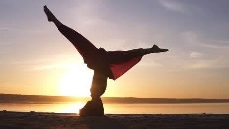 Deportiva-Hermosa-Joven-Mujer-Avanzada-De-Yoga-Parada-En-Sirsasana-Al-Aire-Libre-En-La-Playa.-Hermosa-Puesta-De-Sol,-Silueta