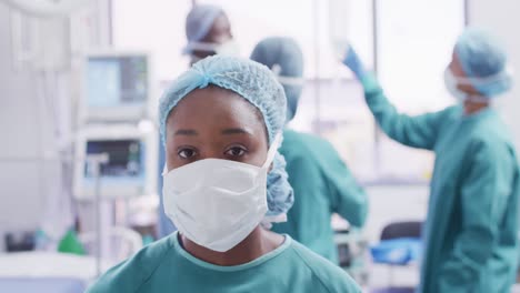 Video-portrait-of-african-american-female-surgeon-in-mask-smiling-in-operating-theatre,-copy-space