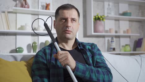 Blind-man-holding-his-white-cane-sitting-on-sofa-at-home.