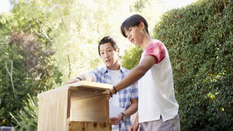 asian father and teenage son working together on wooden project outdoors