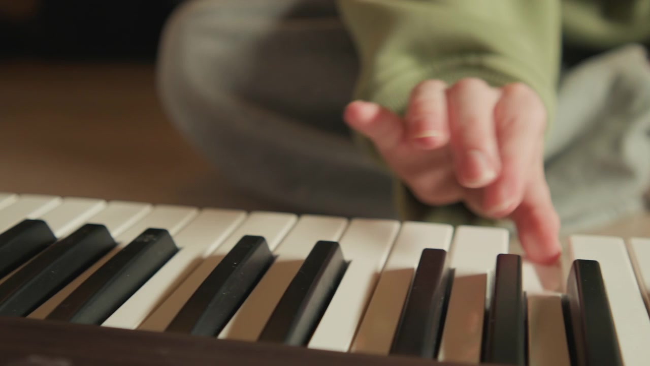 Close view of child s hand in green sleeve pressing white key on electronic keyboard, with clear fingertip contact and downward motion, while soft indoor light and blurred background keep focus on
