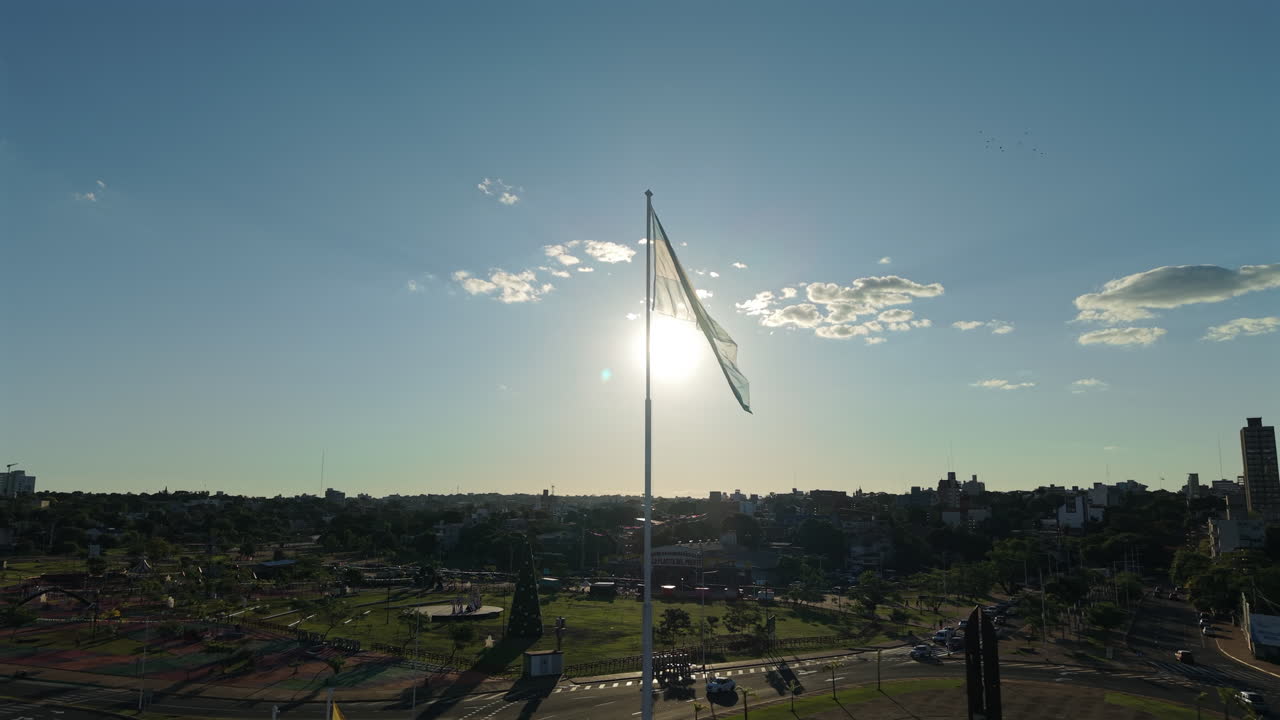vista aérea de la bandera argentina ondeando sobre el horizonte del atardecer y el fondo tranquilo de la ciudad