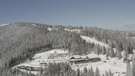 kope ski resort and hotel n the pohorje mountains with visitors on the snowed track, aerial pan right shot