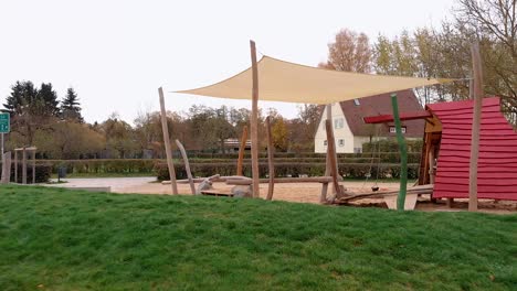 Eine-Drohne-Fliegt-Tief-Durch-Den-Spielplatz,-Fliegt-Weiter-über-Die-Hecke-Und-Dann-über-Den-Rasen