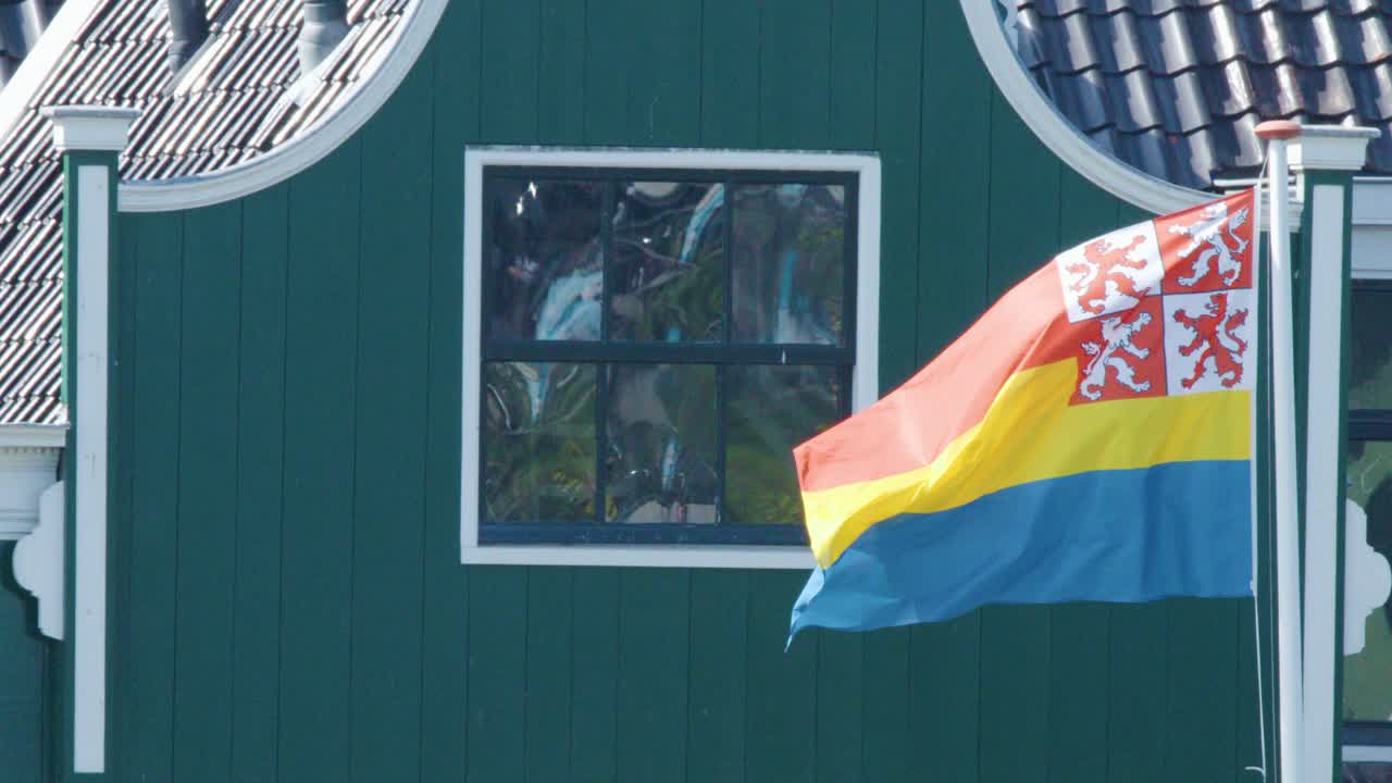 Provincial flag flutters in daylight breeze beside traditional green house, static camera, natural lighting