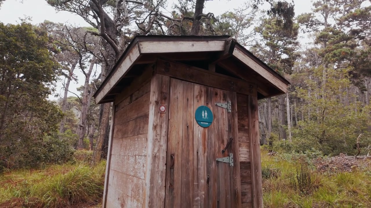 Traditional Wooden Outhouses Standing In A California Park Surrounded By Natural Outdoor Scenery. Tilt-down Shot