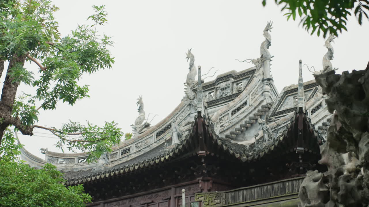 Pavillontag indrammet af havens løvtag, lagdelte tagudhæng og silhuetten af en stenhave, bredt udsyn fanger udsmykkede spir, mosbegroede sten- og trædetaljer for en filmisk, historisk stemning.