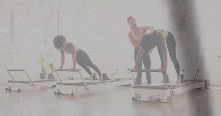 Instructor placing hand and giving cues, adjusting student alignment over reformer bar for Pilates