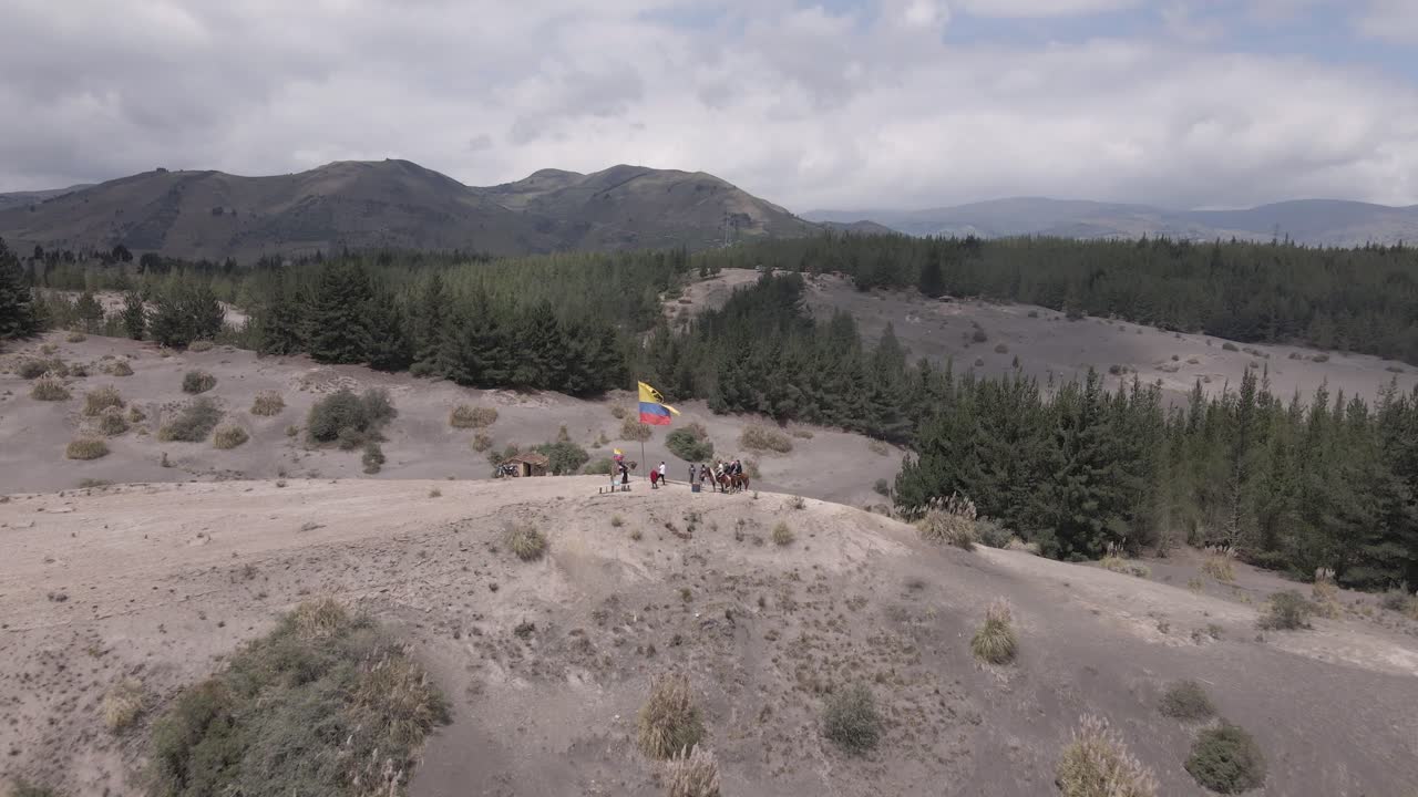 People ride horseback in desert hill with torn flag of Columbia