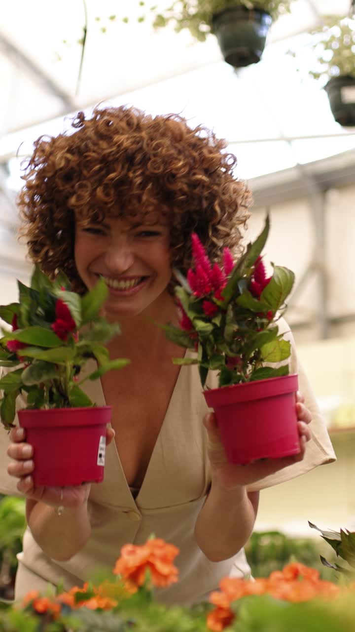 Woman gardener holding and smelling potted flowers in greenhouse. Vertical