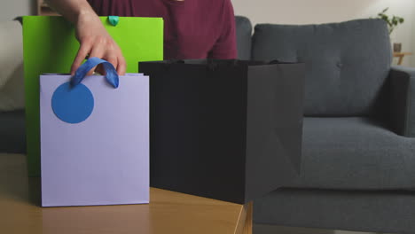 close up of man taking gift wrapped presents out of bags with tag on table in lounge at home