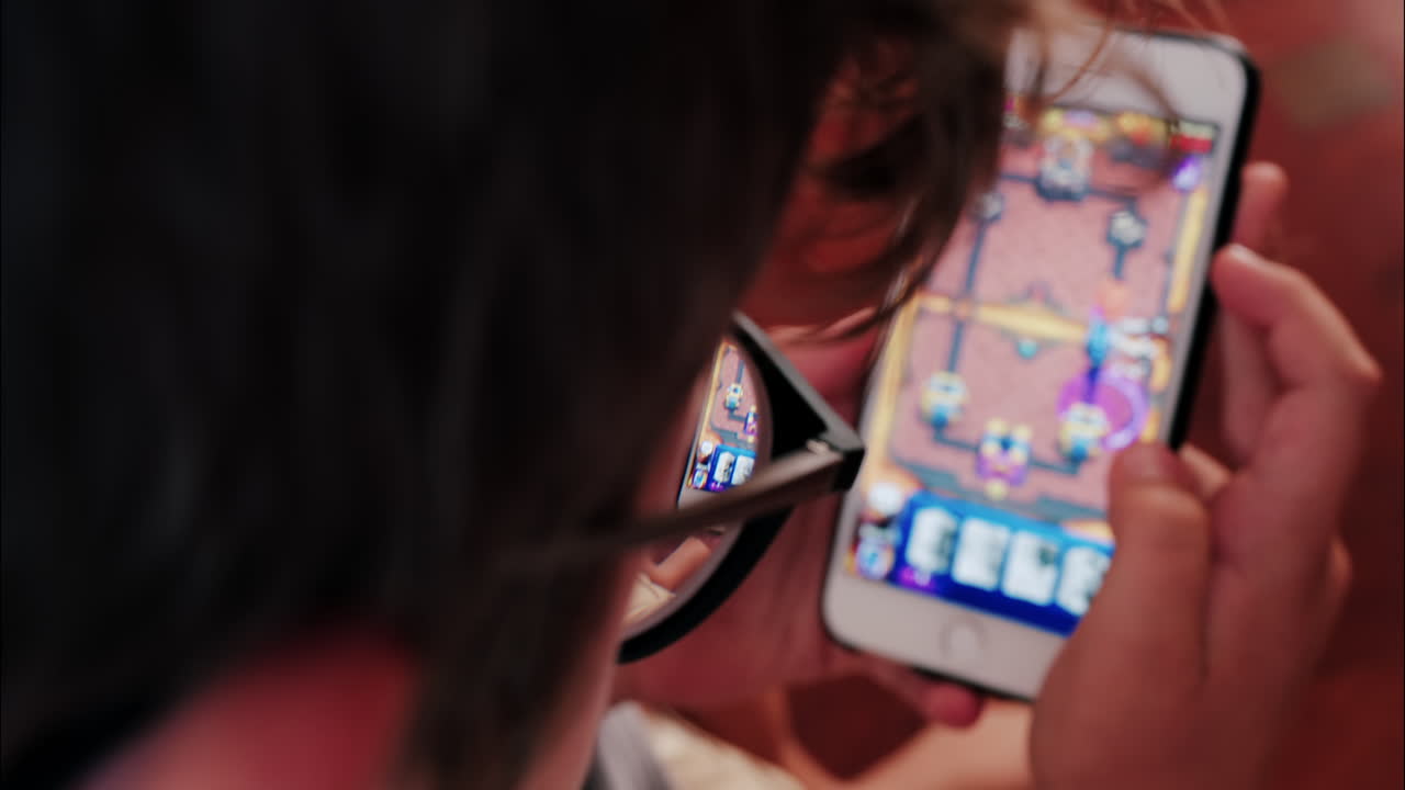 Over-the-shoulder close-up of a kid with glasses playing on a smartphone indoors