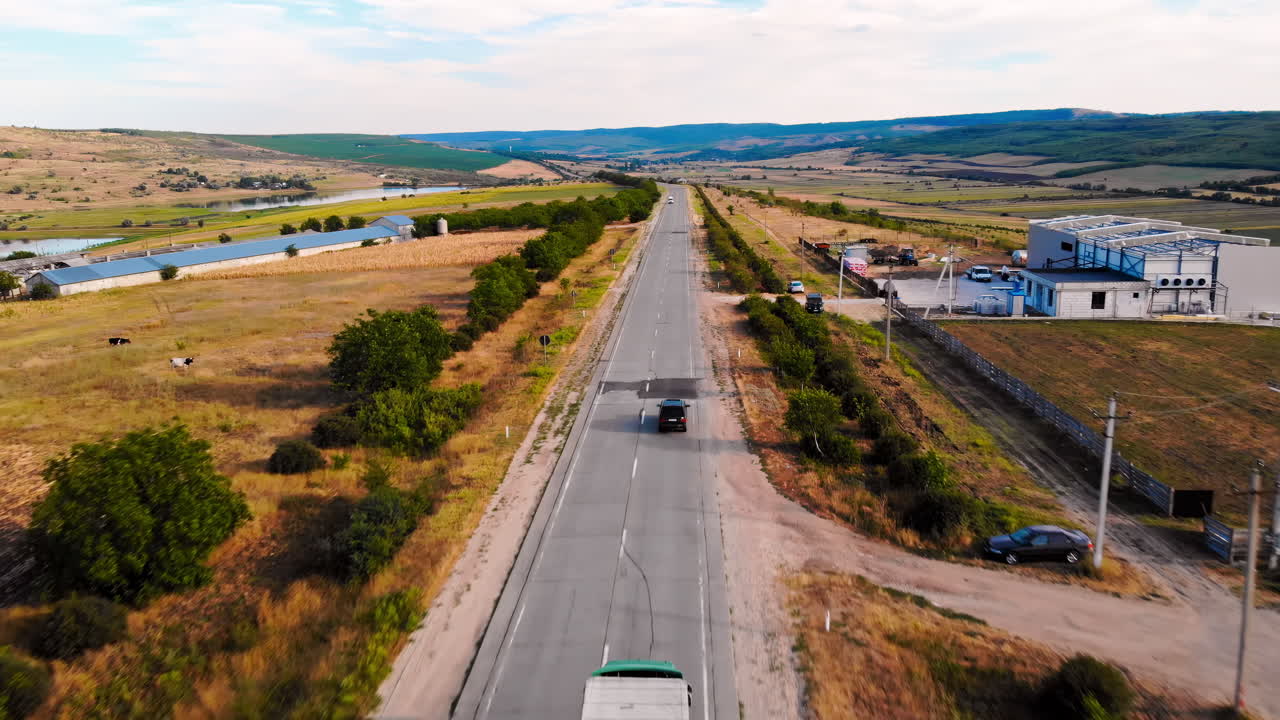 Aerial drone view of a road with moving cars in highland. Small village and green hills on background. Sunny day. Balti, Moldova