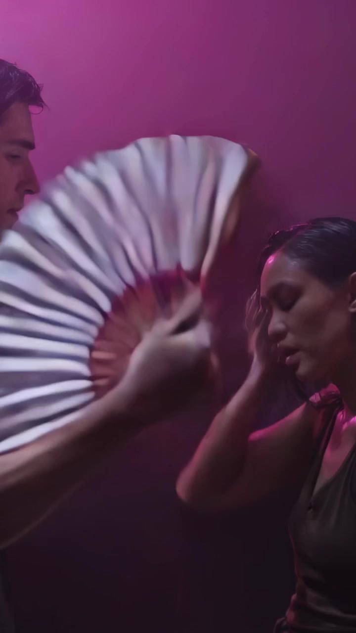 Video verticale: Notando una donna in canotta che respira, un uomo agita un ventaglio, rinfrescandola nella foschia del club.