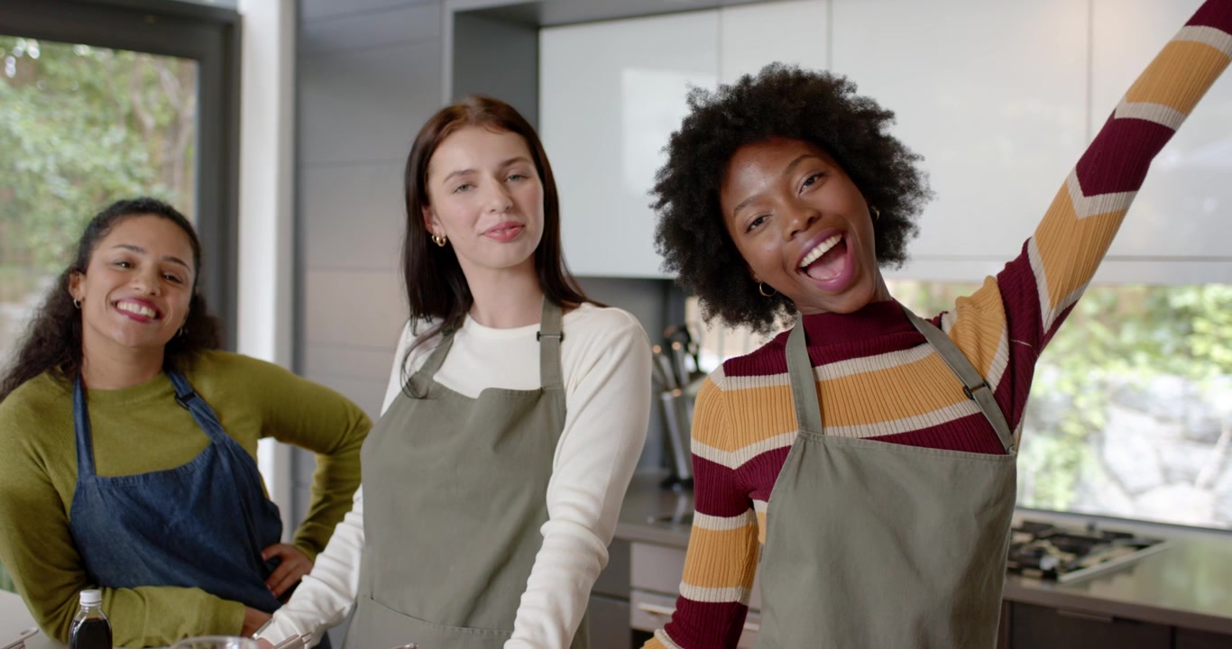 Amiche diverse che riprendono una ricetta sull'isola della cucina, con ciotole e grembiuli