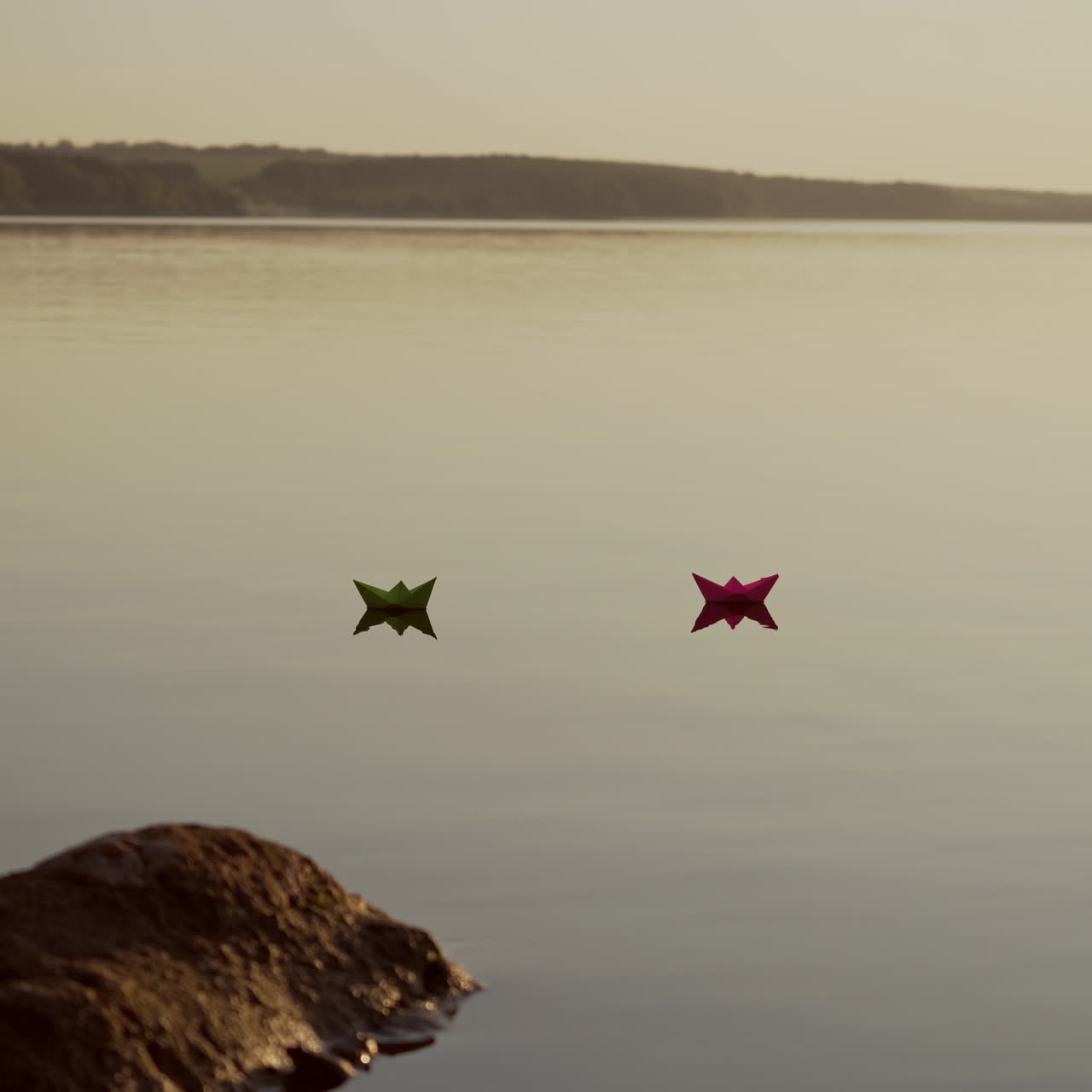 Red and green Paper Ships in the river. Origami Paper Boats are Sailing in the lake. Beautiful Waves Ripple Background. Unusual Travel Concept. Filtered video.
