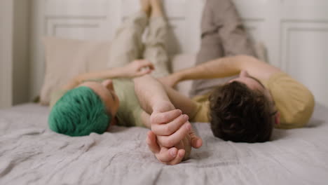 loving couple holding hands and looking at each other while lying on a cozy bed with their legs up on the wall 1