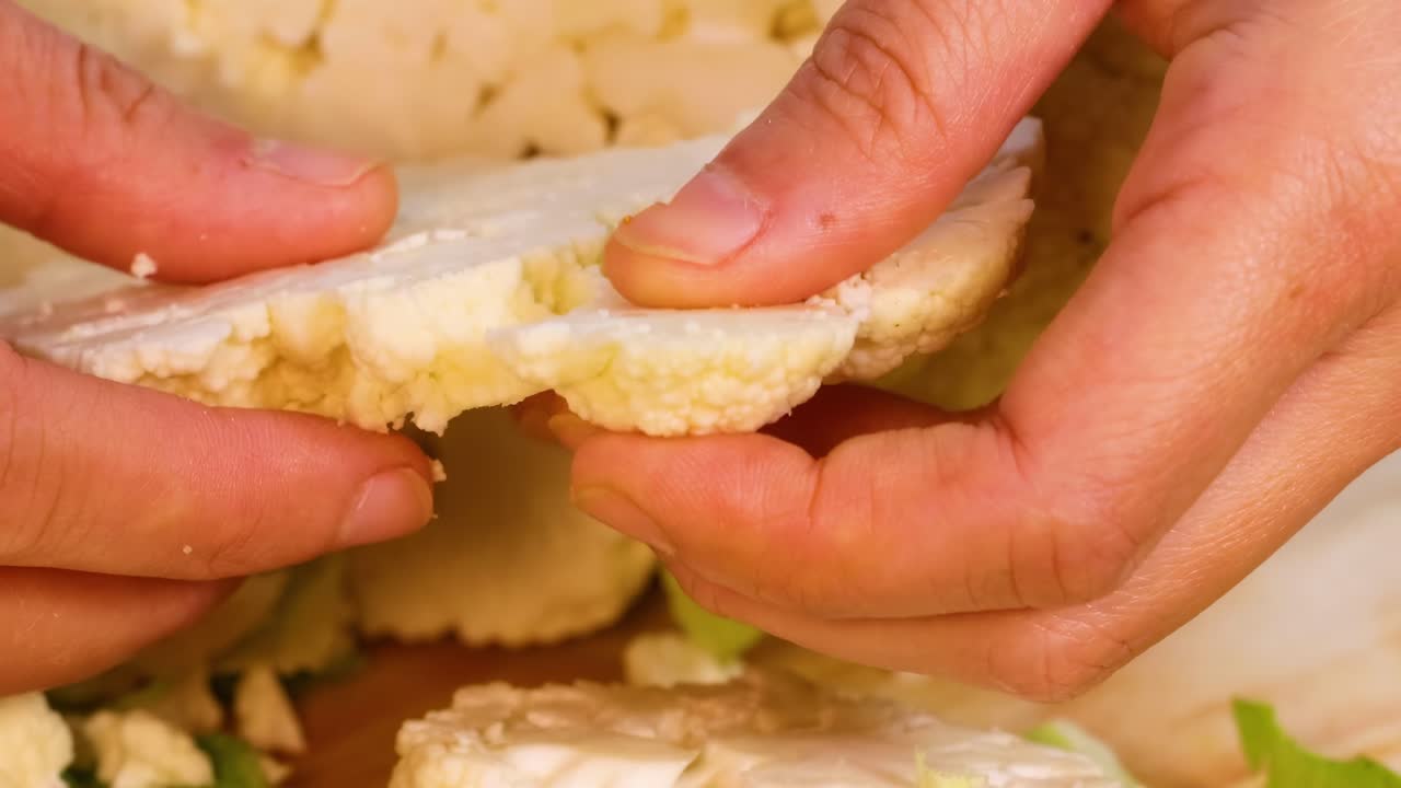 Close-up of hands carefully separating cauliflower florets on a wooden surface.