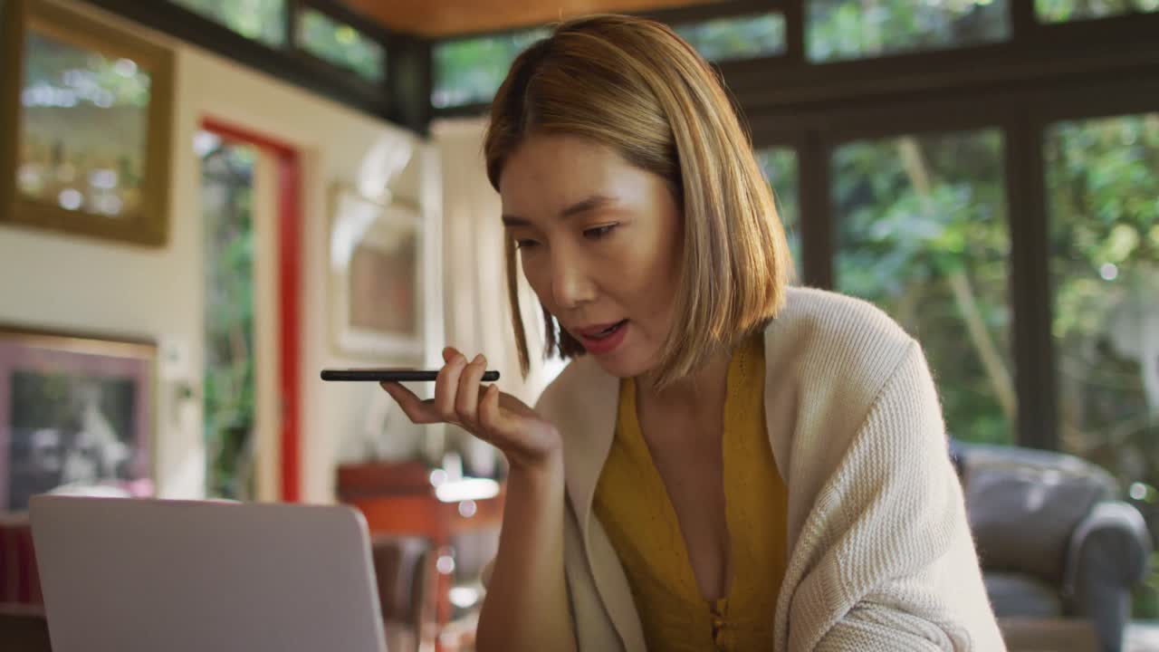 집에서 스마트폰과 노트북을 사용하여 일하는 테이블에 앉아 있는 아시아 여성