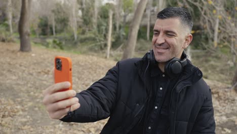 Un-Hombre-Sostiene-Su-Teléfono-Tomando-Selfies,-Grabando-Historias-O-Haciendo-Una-Videollamada-Mientras-Camina-Por-El-Bosque