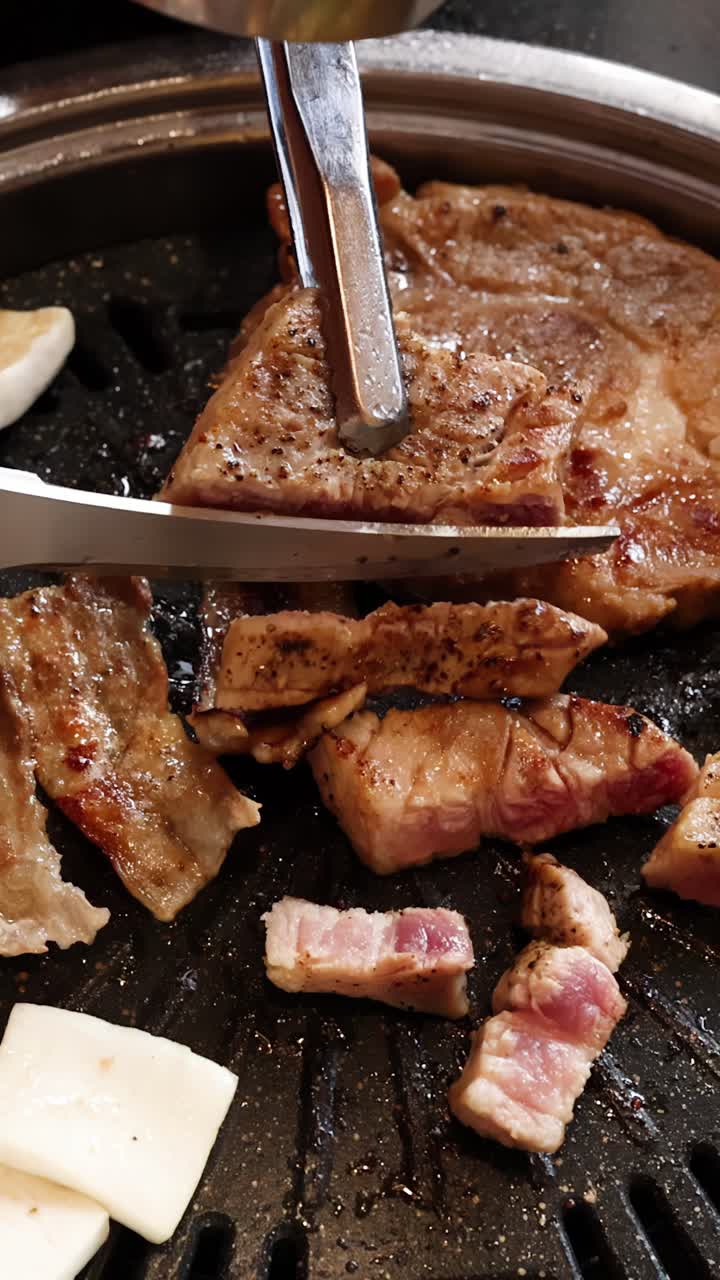 Tangan menggunakan penjepit dan gunting untuk memotong perut babi di atas panggangan barbekyu Korea, tampilan atas.