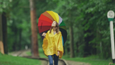 hübsches mädchen in einem gelben regenmantel, das mit einem regenschirm im regen spaziert