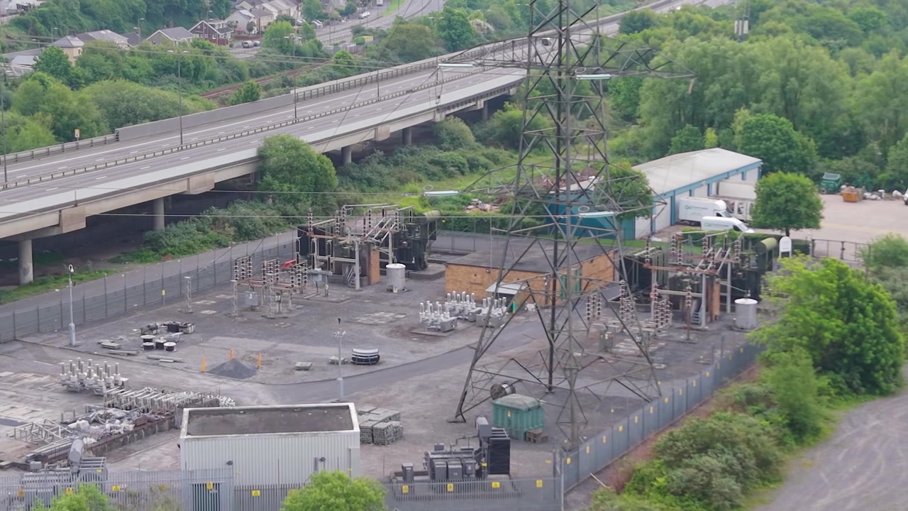 Luchtfoto van een hoogspanningsstation met hoogspanningsmast nabij een snelweg. Kritieke infrastructuur van een modern elektriciteitsnet, energiedistributie, industriële techniek. Wales, VK. 4K.