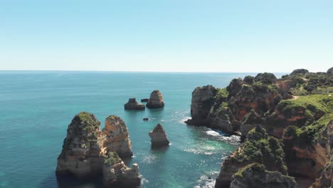 Rocky-protuberances-rising-from-the-salty-Algarvian-sea,-in-Lagos-coastline,-Portugal---Aerial-wide-Crane-down-shot