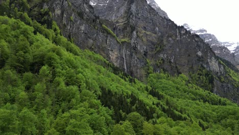 Beautiful-aerial-shot-of-waterfall-nestled-in-rocky-mountain,-Alpine-forest