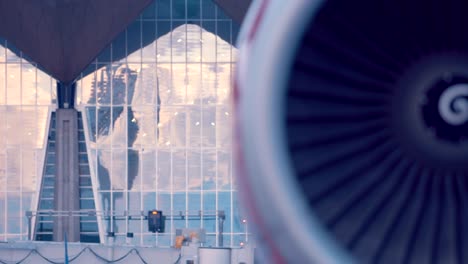 the plane is standing next to the airport building, the red turbine rotates