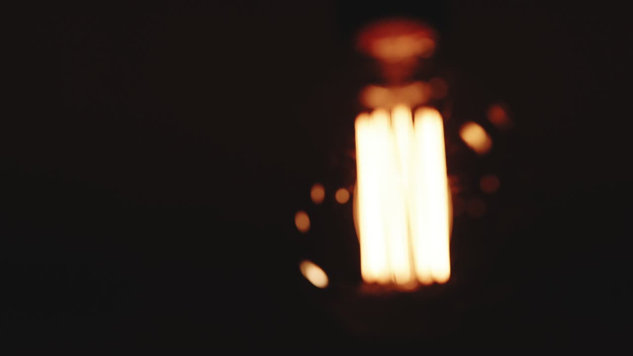 Light bulb Warm yellow light over dark black background. Bright glowing Edison Tungsten lamp. Retro vintage form. Creative idea concept. Close-up Of A Tungsten Light Bulb Switching On