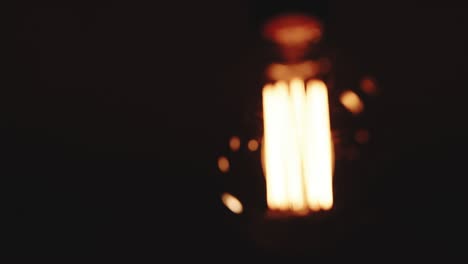 light bulb warm yellow light over dark black background. bright glowing edison tungsten lamp. retro vintage form. creative idea concept. close-up of a tungsten light bulb switching on