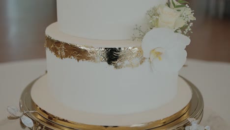 cerca de un elegante pastel de boda blanco adornado con detalles de hoja de oro y flores blancas frescas