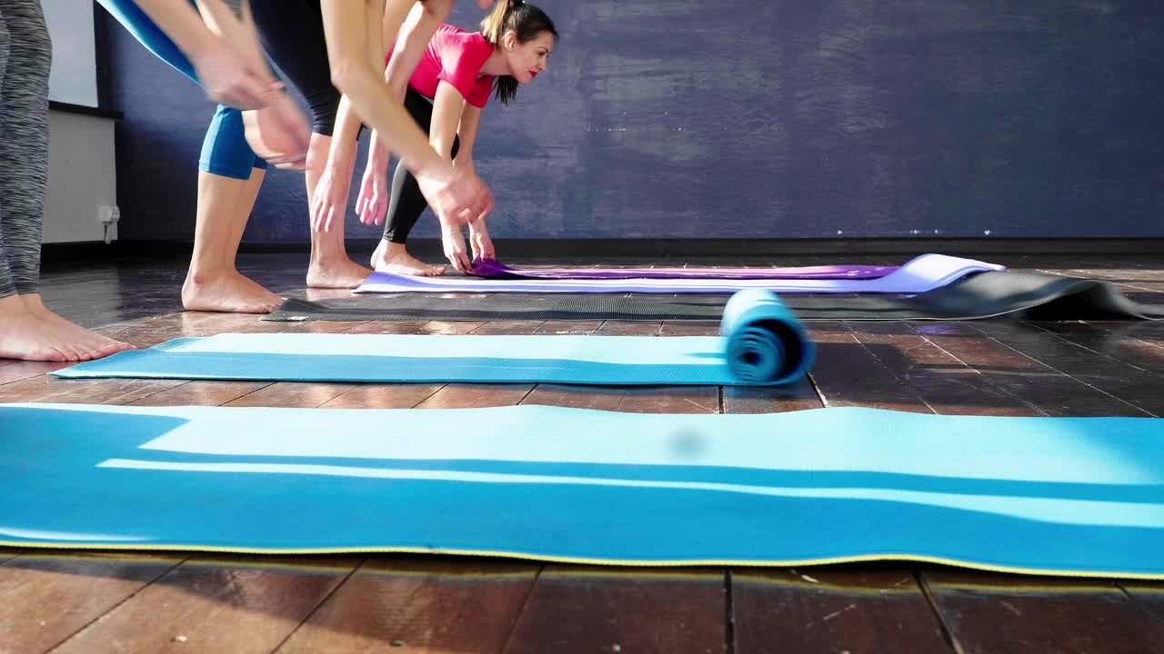 Women rolling out yoga mats in studio