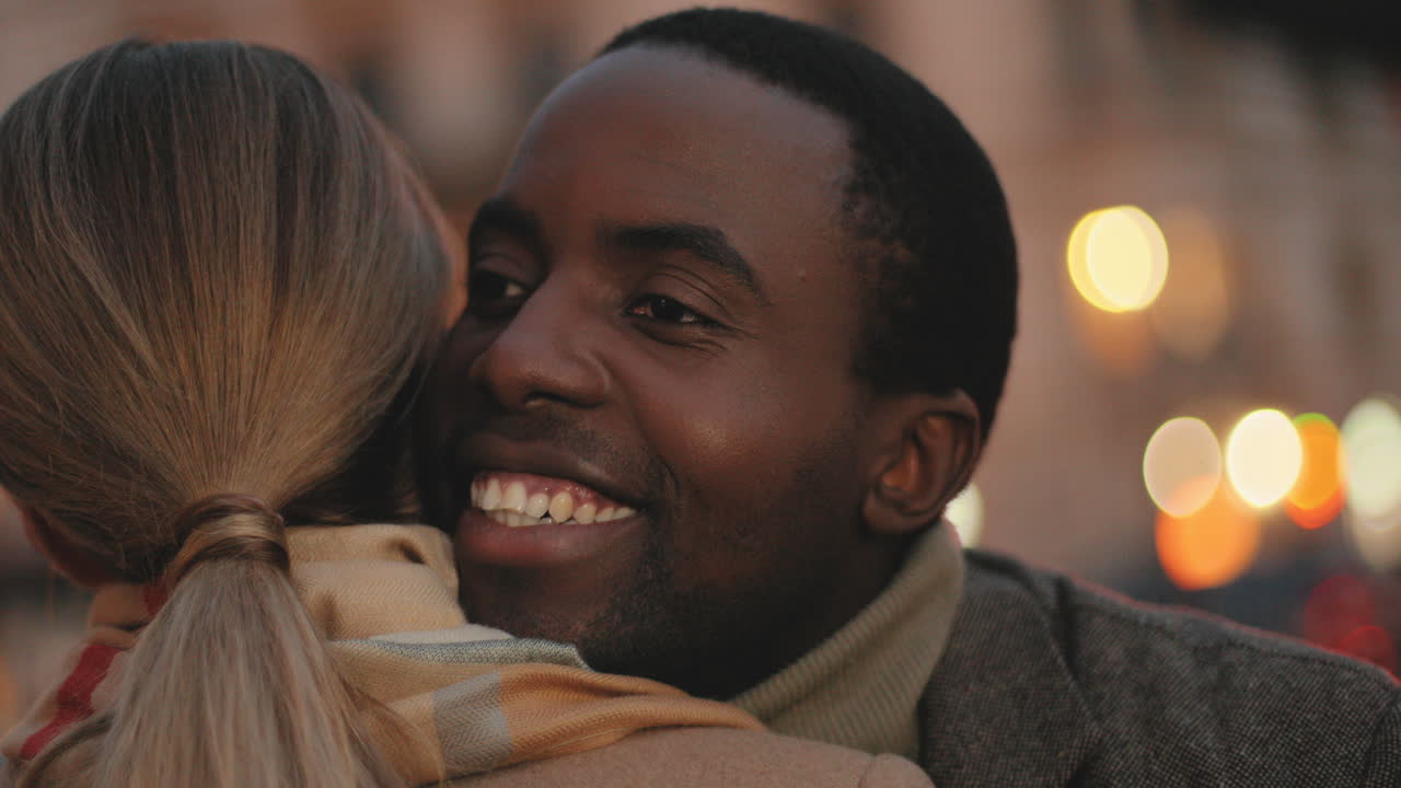 Rear view of young caucasian woman hugging a african american smiling man in the street in the evening