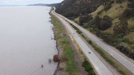 drone descending near a lake and a 4 lane motorway where cars are passing by