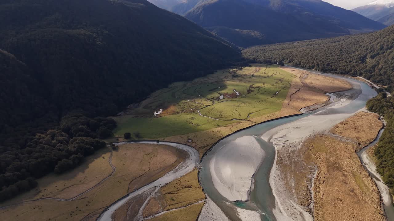 Breathtaking aerial view of New Zealand's stunning landscapes. Winding river flows through lush green fields, framed by majestic mountains. Wide shot
