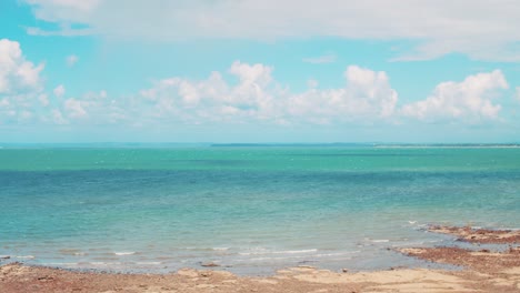 timelapse of fluffy white clouds billowing above a tropical blue, rocky beach that looks over the vast ocean harbouring small islands and boats