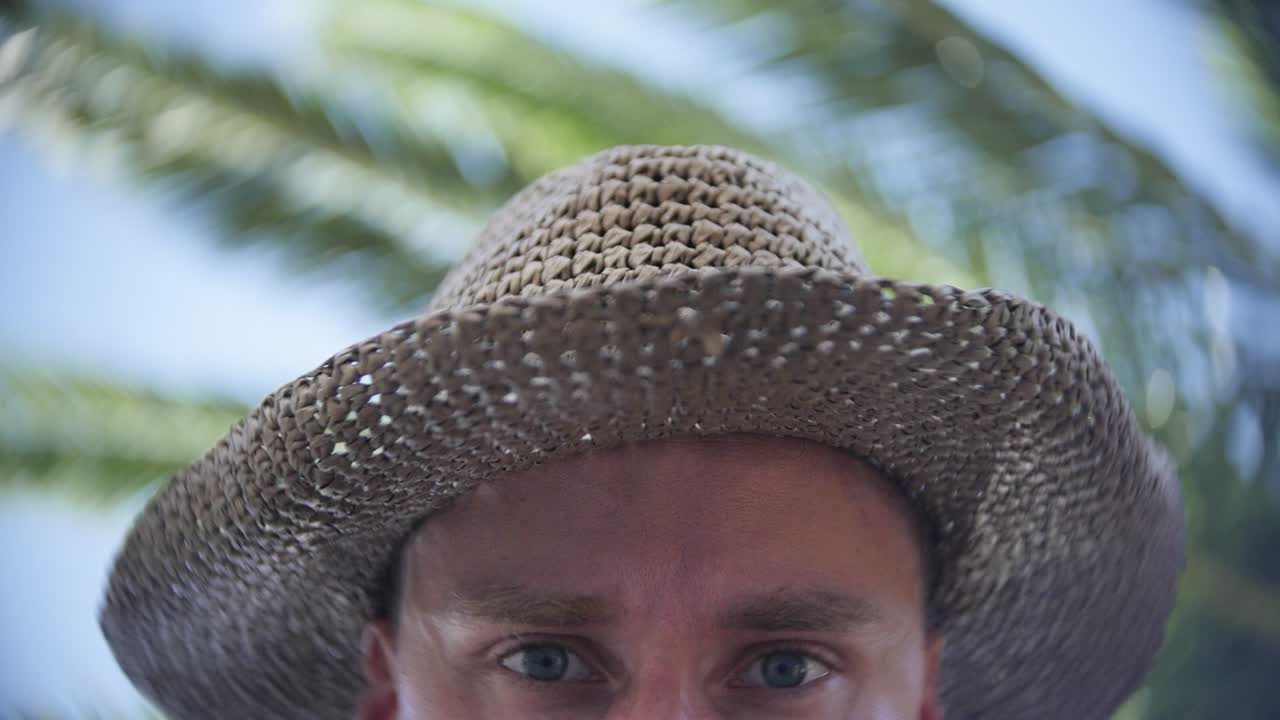 A person wearing a woven straw hat with palm trees and a blue sky in the background, exuding a tropical and relaxed vibe.