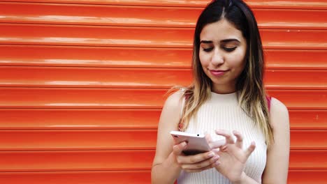 cámara lenta: hermosa joven usa un teléfono inteligente frente a un fondo naranja y rojo
