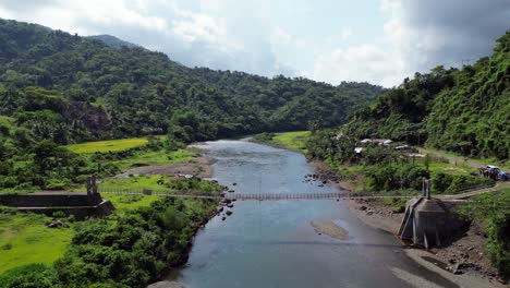 Handcart-is-pushed-across-a-suspension-bridge-crossing-a-tropical-river-in-forest-valley