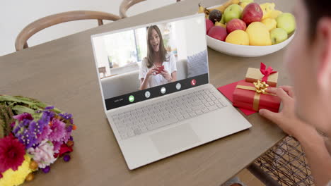 Caucasian-woman-holding-red-gift-using-laptop-with-caucasian-woman-on-screen