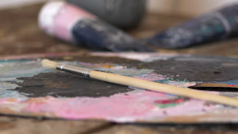 Slow-close-up-pan-of-thin-wooden-painting-brush-on-color-palette