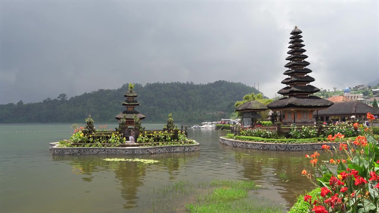 Wunderschöner Ulun Danu Bratan Tempel am See, Bali. Halbtotale, Schwenk von links nach rechts. Blumen und Spiegelungen auf dem Wasser.